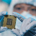 A technician wearing cleanroom apparel and holding a microchip.